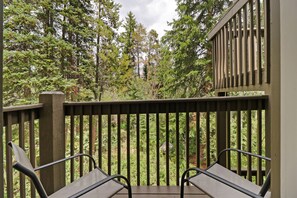 Une terrasse en bois avec deux chaises en métal, entourée d’un feuillage verdoyant et luxuriant.