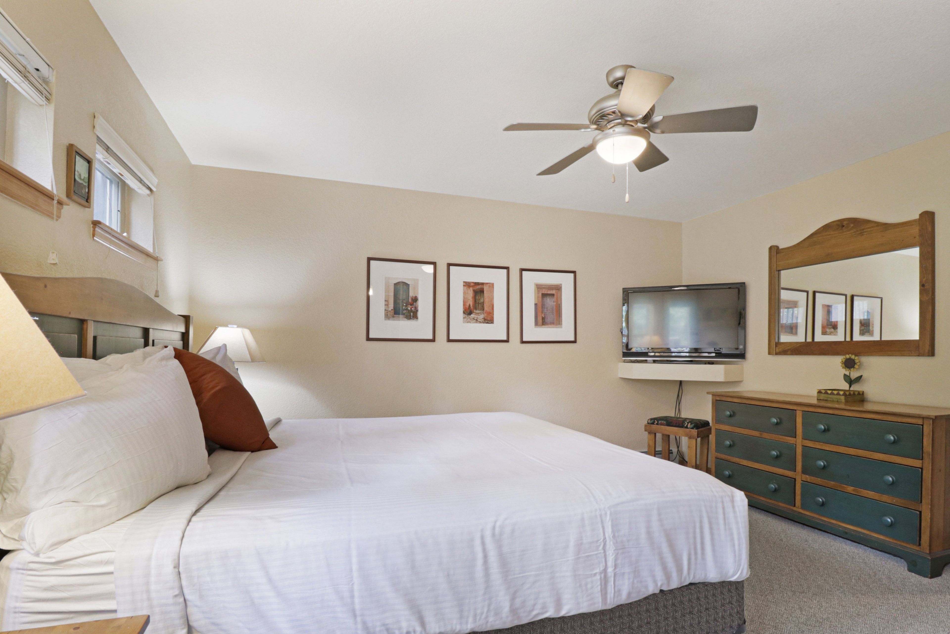 A hotel room with a bed, a television, a dresser, and a ceiling fan.