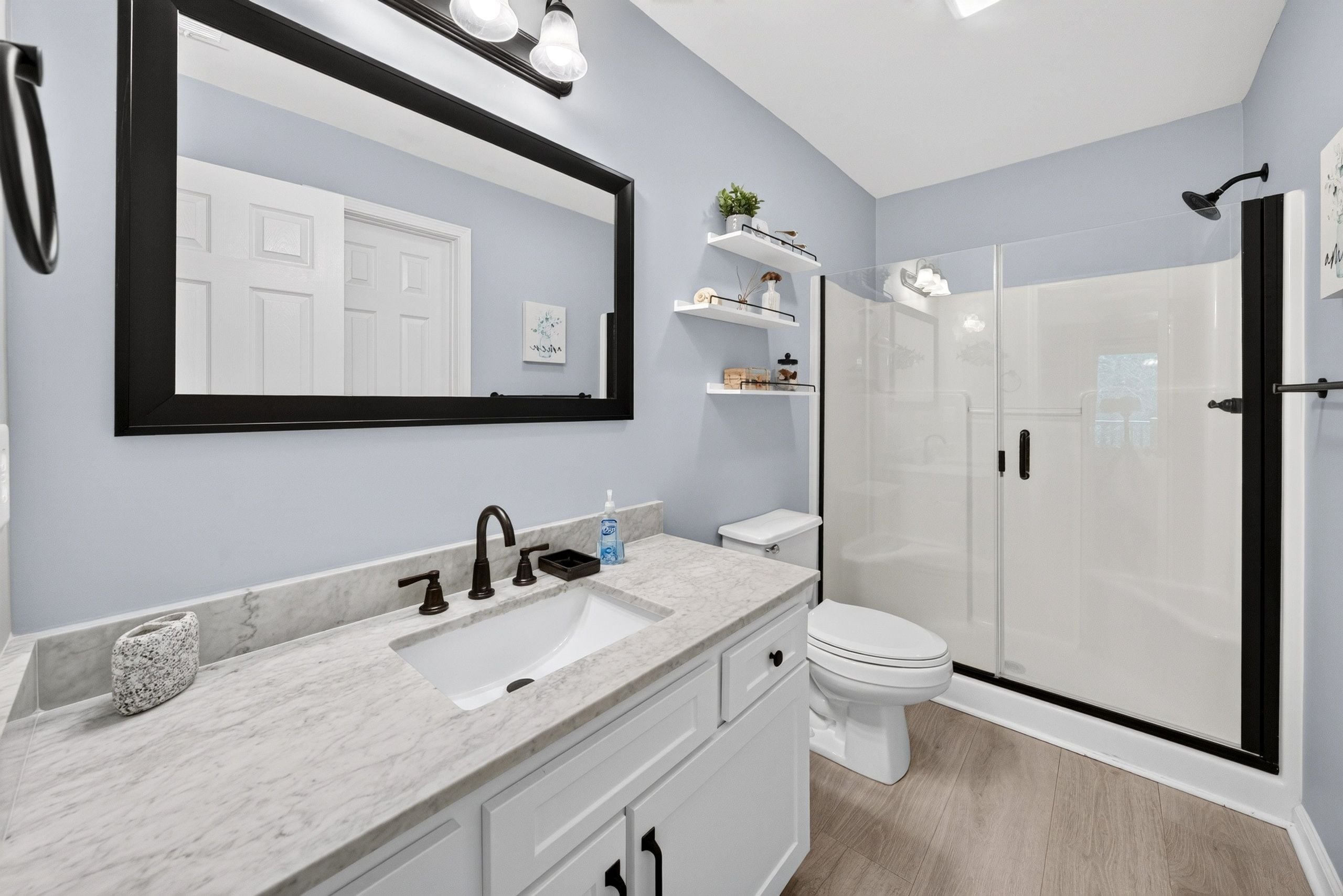 A modern bathroom with a marble sink, a toilet, a glass shower enclosure, and a large mirror with lights.