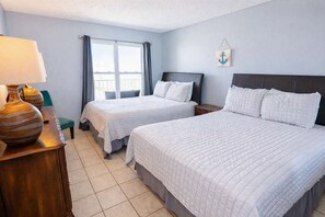 Quarto de hotel com duas camas, uma mesa de cabeceira, uma luminária e uma janela com cortinas.
