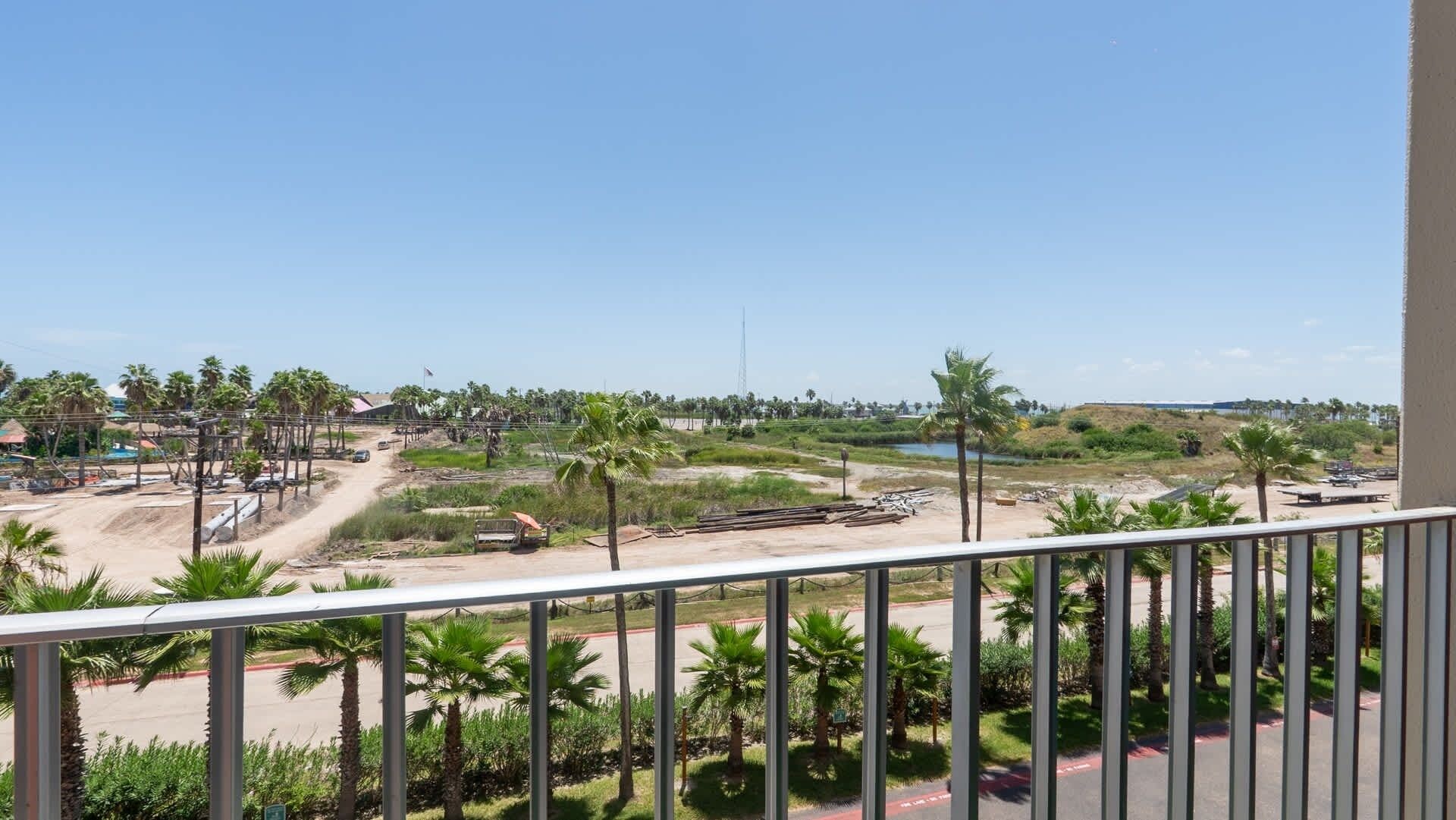 Un balcón con vista a una obra en construcción, palmeras y un cielo despejado.