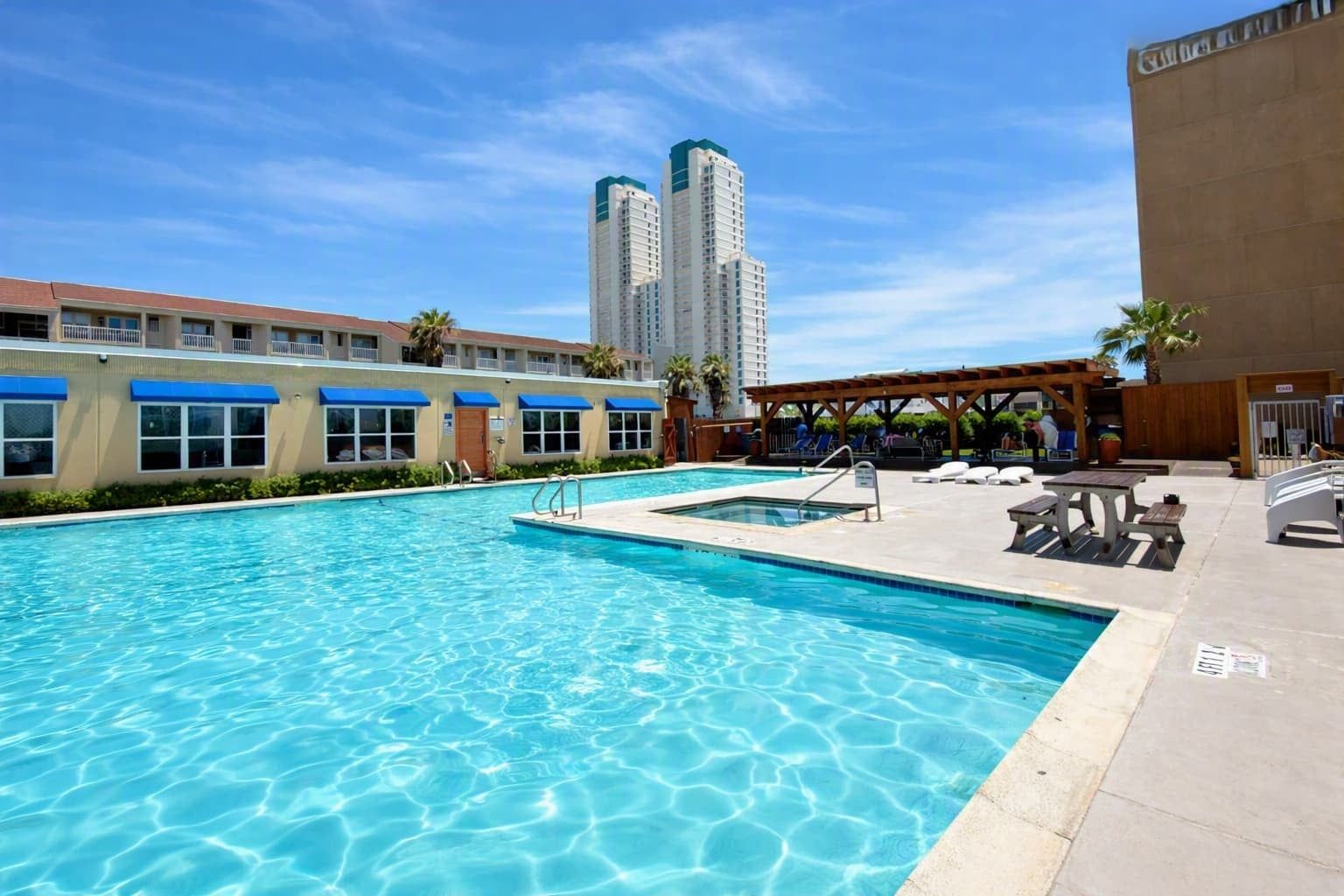 A swimming pool with a sun deck, lounge chairs, and a view of tall buildings in the background.
