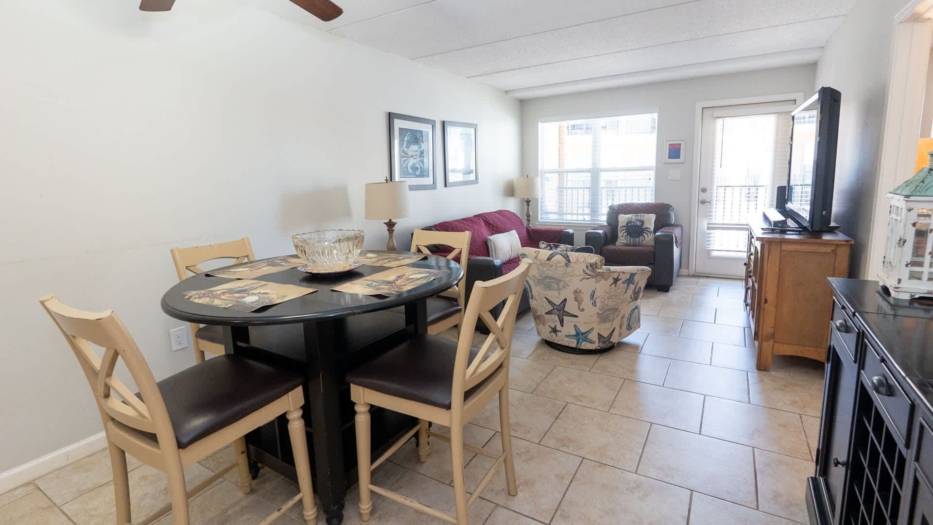 A dining area with a round table, chairs, and a bowl. There is a sofa and a chair in the background.