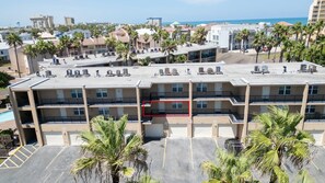 A multi-story hotel with a rooftop pool area, palm trees, and a view of the ocean. - 2br Half Block To Beach, Garage, Heated Pool 2 Bedroom Apts (South Padre Island)