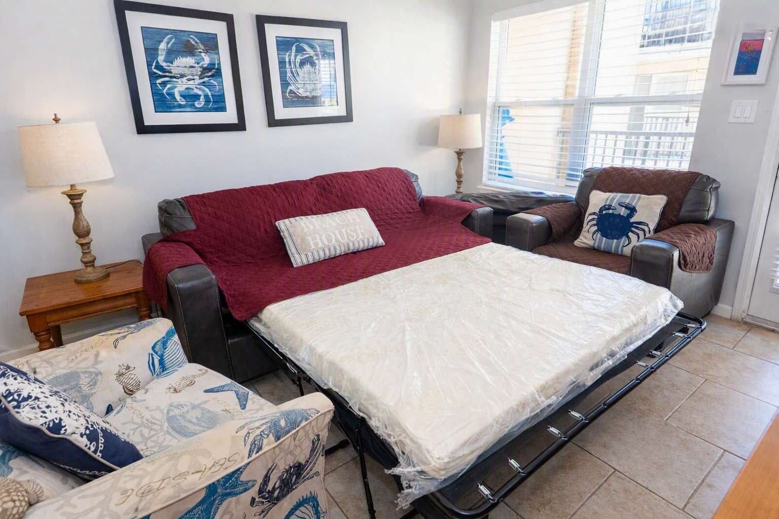 A room with a bed, two chairs, a table, and artwork on the wall.