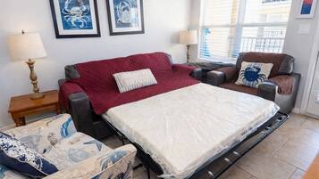 A room with a bed, two chairs, a table, and artwork on the wall.