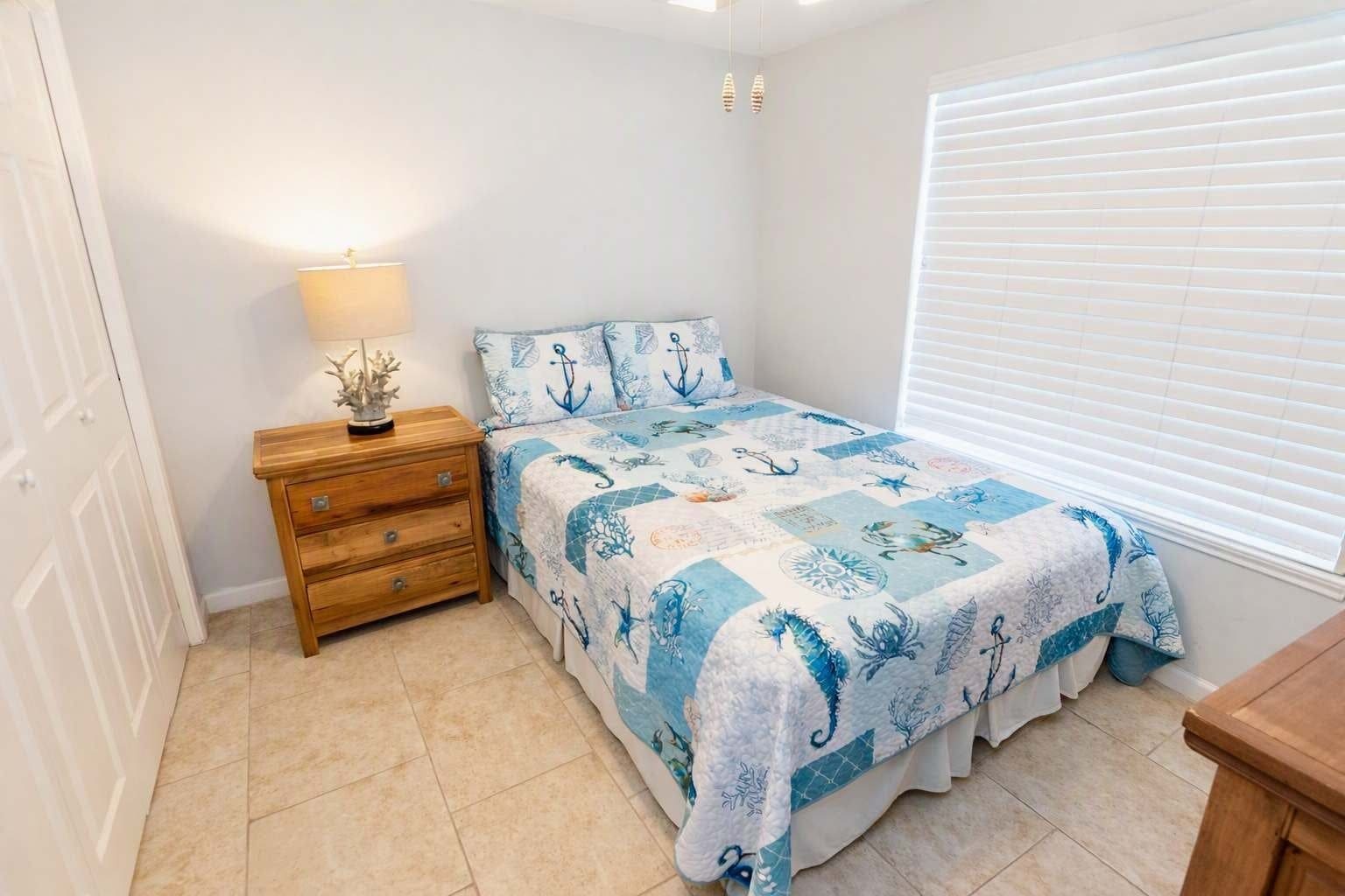 A bedroom with a bed, a nightstand, a lamp, and a window with blinds.