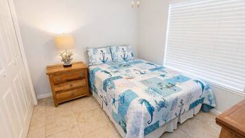 A bedroom with a bed, a nightstand, a lamp, and a window with blinds.