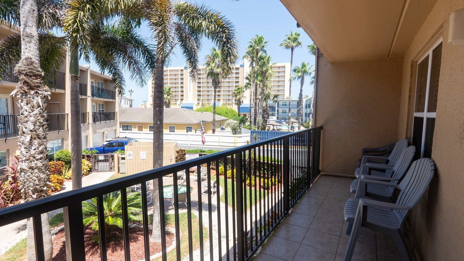A balcony with a view of a parking area, palm trees, and a building in the background.