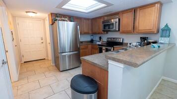 A kitchen with a stainless steel refrigerator, microwave, and stove, wooden cabinets, a granite countertop, and a skylight.