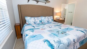 Quarto com cama, mesa de cabeceira, abajur e um enfeite de peixe na parede.