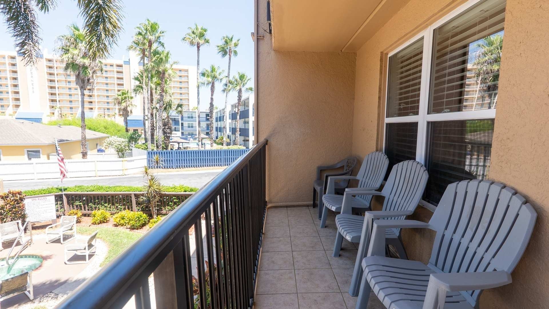 A balcony with chairs and a view of palm trees and buildings.