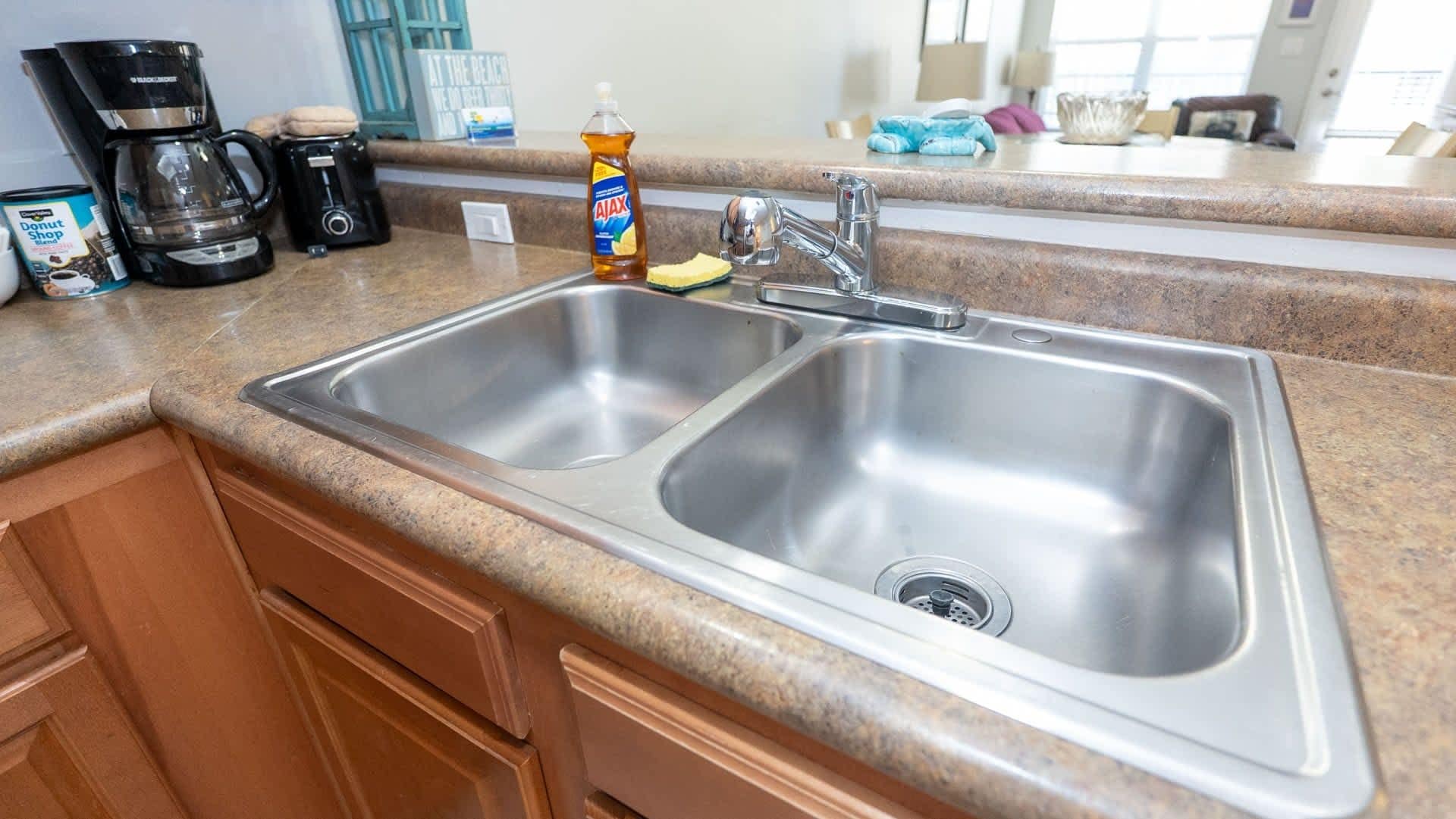 A kitchen with a double stainless steel sink, a coffee maker, and a bottle of Ajax dish soap.