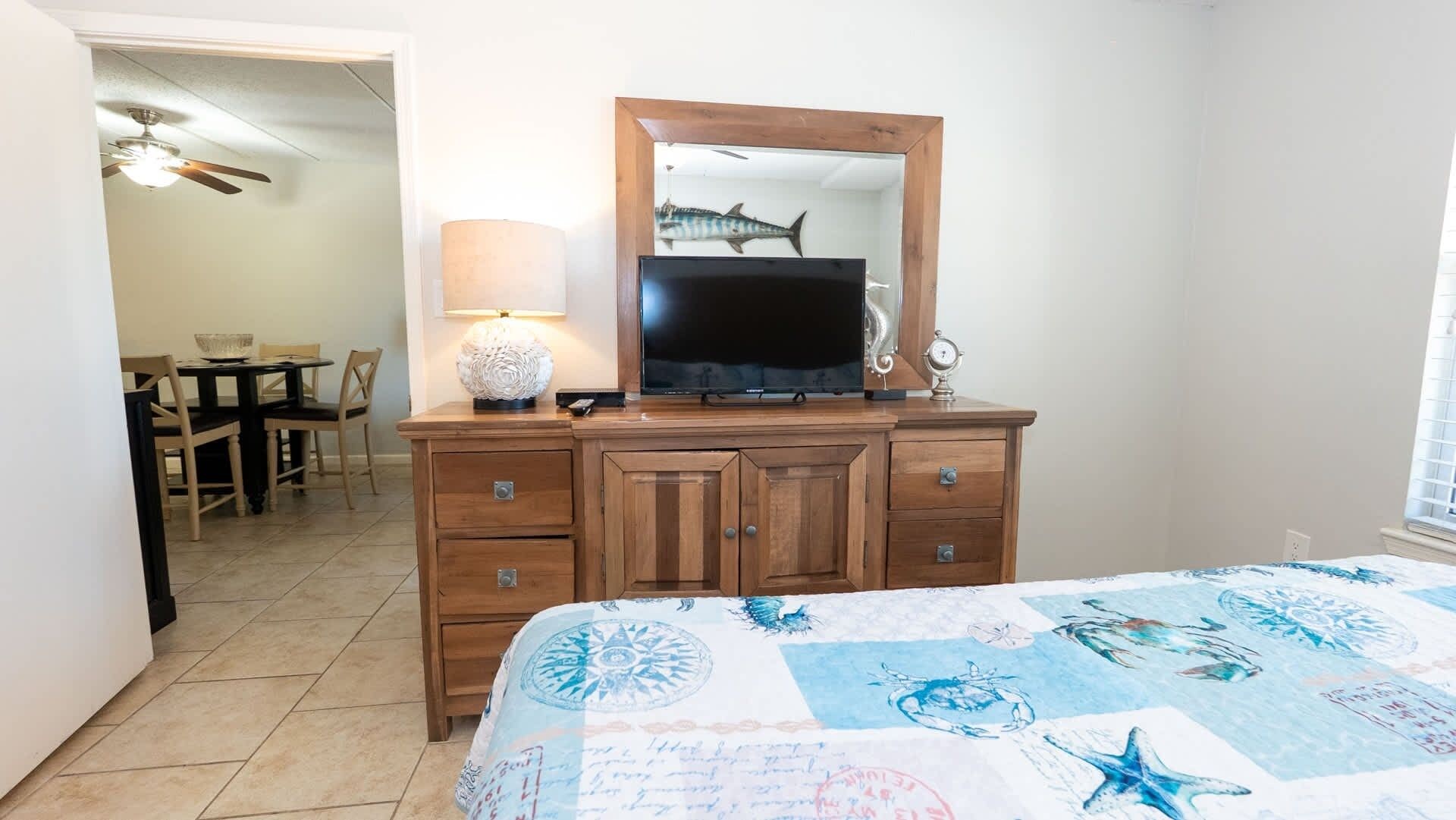 Un dormitorio con una cama, un aparador con espejo, un televisor y una lámpara.