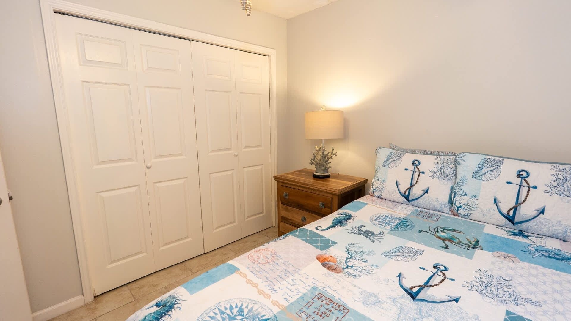 Een slaapkamer met een bed, nachtkastje, lamp en een kledingkast.