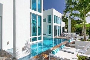 Zona de piscina moderna amb una piscina cristal·lina, gandules blanques i una palmera.