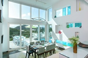 A modern dining area with a glass table and chairs, large windows, and a view of the outdoors. - Casa Mare – Modern 5-Bedroom St. John Villa with Private Pool, Ocean Views & Rooftop Stargazing (cruz bay)
