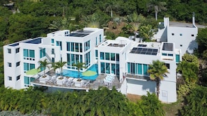 A modern multi-story building with solar panels, a swimming pool, and lounge chairs. - Casa Mare – Modern 5-Bedroom St. John Villa with Private Pool, Ocean Views & Rooftop Stargazing (cruz bay)