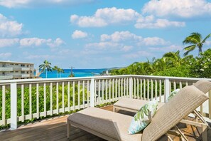 A wooden deck with two lounge chairs and a railing, overlooking a clear blue ocean and a resort area. - Kauai Hoohu Hale 3 Bedroom Home (Koloa)