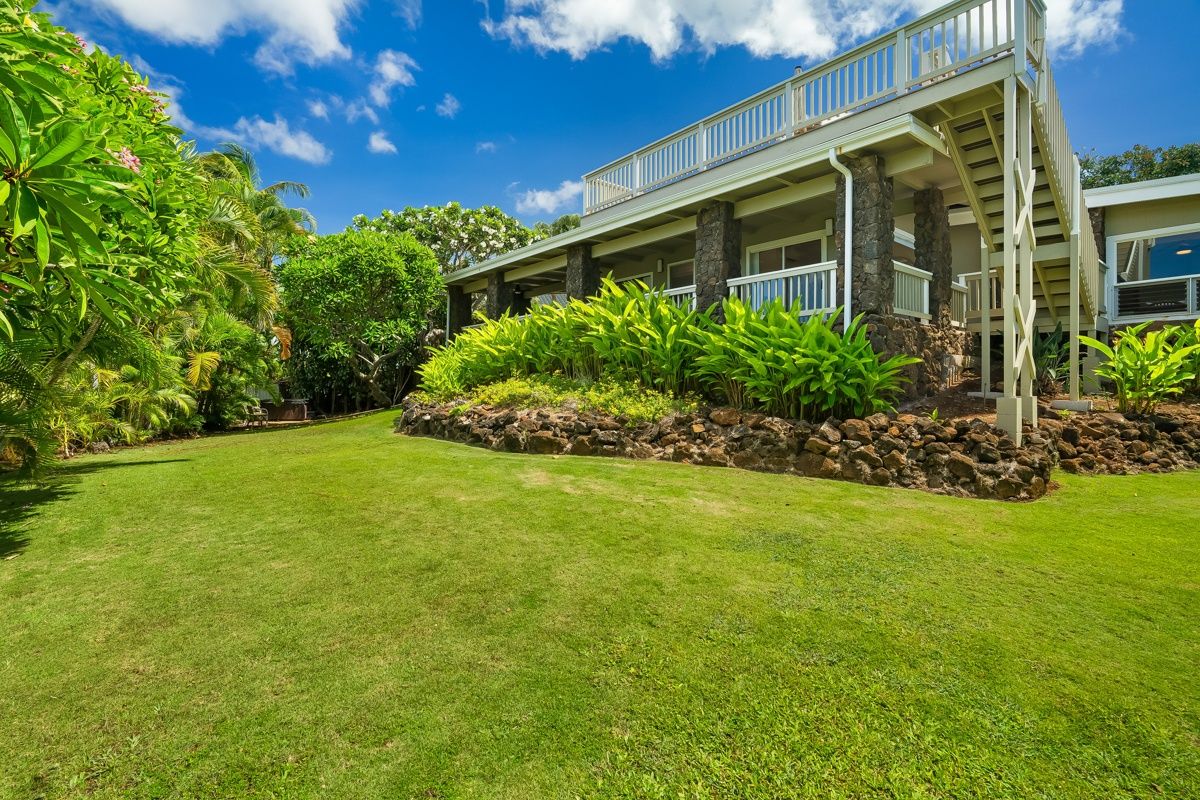 A two-story house with a balcony, surrounded by lush greenery and a well-maintained lawn.