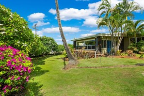 A residential property with a well-maintained lawn, palm trees, and a house with large windows. - Kauai Hoohu Hale 3 Bedroom Home (Koloa)