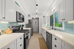 A modern kitchen with white cabinets, stainless steel appliances, and a view of greenery through a window. - Kauai Hoohu Hale 3 Bedroom Home (Koloa)