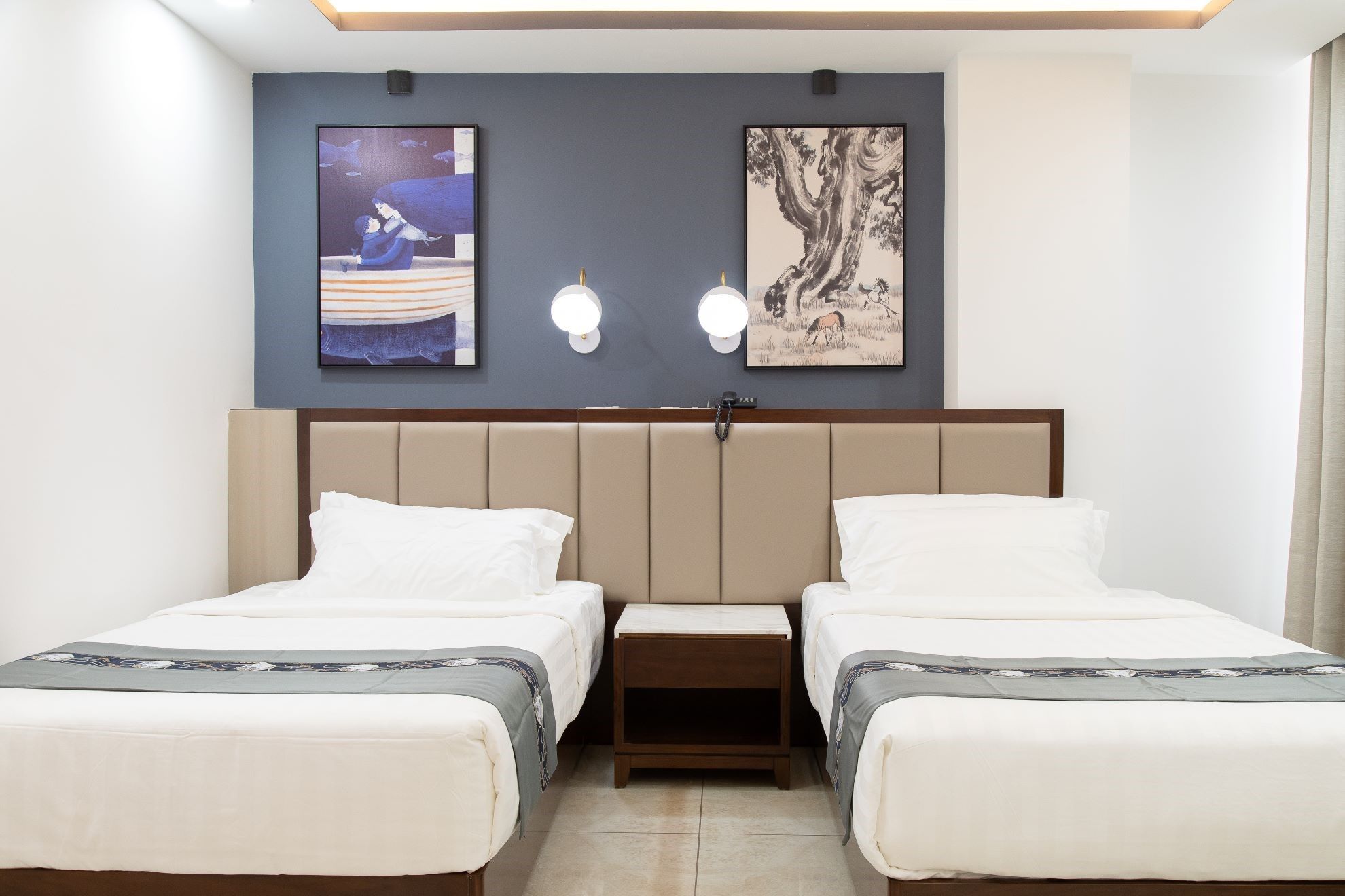 Habitación de hotel con dos camas, cabeceros, mesitas de noche y una obra de arte en la pared.