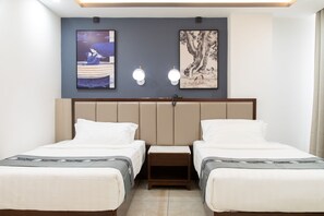 A hotel room with two beds, a headboard, bedside tables, and artwork on the wall.