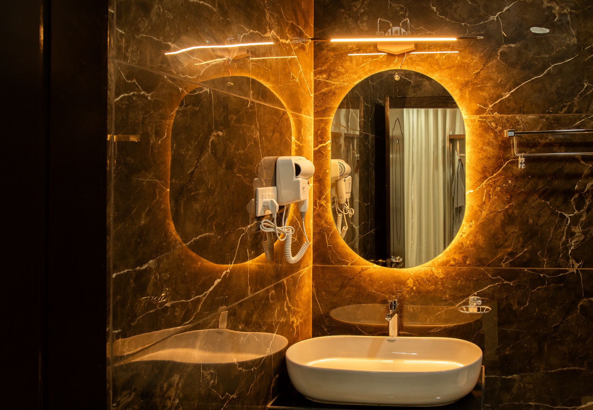 A bathroom with a marble wall, a round mirror, a sink, and a hairdryer.