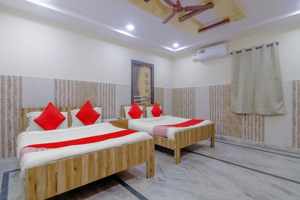Une chambre d’hôtel avec deux lits en bois, des oreillers rouges, un ventilateur de plafond, un appareil de climatisation et des rideaux à motifs.