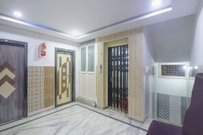 A hallway with three doors, a fire extinguisher, and a patterned floor. - Classic Hotel Ashoka Grand (Sadasivpet)