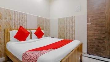 Una habitación de hotel con una cama, dos almohadas rojas, una colcha blanca y un cabecero de madera.