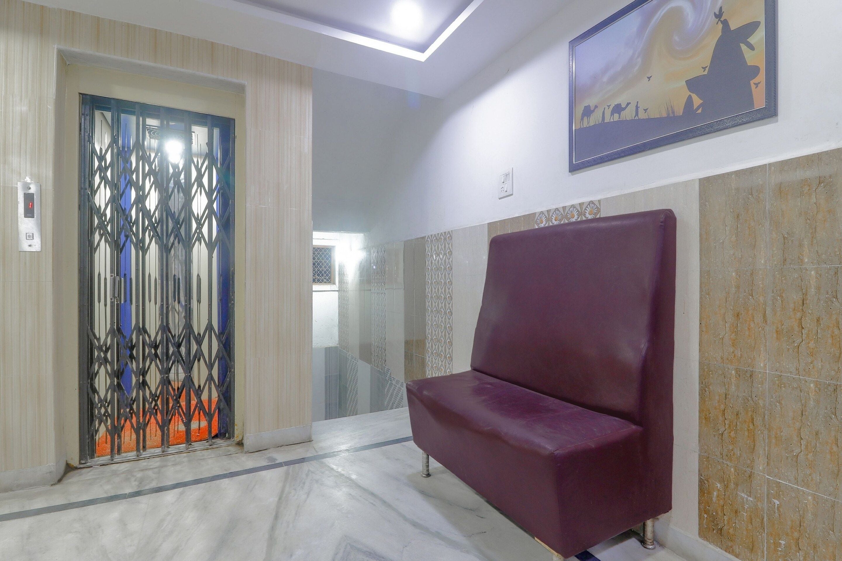 A reception area with a marble floor, a red cushioned bench, a decorative door, and a framed artwork on the wall.
