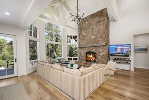 A modern living room with a stone fireplace, large windows, and a cozy seating area. - Exceptional Arrowhead Riverfront Retreat | Hot Tub & 2-Car Garage (Edwards)