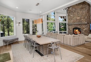 A modern kitchen with a large island, dining area, and a stone fireplace. - Exceptional Arrowhead Riverfront Retreat | Hot Tub & 2-Car Garage (Edwards)