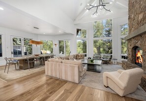 A spacious living room with a fireplace, large windows, and a modern chandelier. - Exceptional Arrowhead Riverfront Retreat | Hot Tub & 2-Car Garage (Edwards)