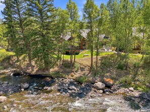 A river flowing through a forest with a house in the background. - Exceptional Arrowhead Riverfront Retreat | Hot Tub & 2-Car Garage (Edwards)