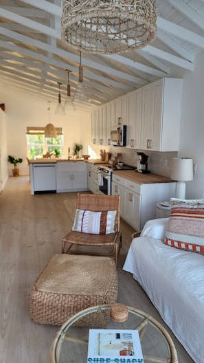 A cozy room with a wicker chair, a bed with a striped pillow, a glass coffee table with a magazine, and a kitchen in the background. - 2-Bedroom Nature Lovers Escape (Sanibel)