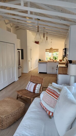 A modern living room with a sofa, a wicker chair, and a kitchen in the background. - 2-Bedroom Nature Lovers Escape (Sanibel)