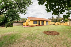 Una casa amarilla con techo rojo, rodeada de un césped cuidado y un árbol.