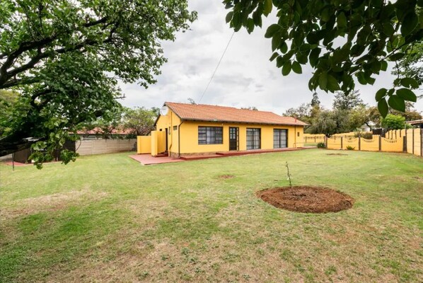 Une maison jaune avec un toit rouge, entourée d’une pelouse bien entretenue et d’un arbre.