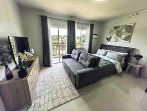 A bedroom with a sofa bed, a flat-screen TV, a dresser, and a painting on the wall. - Stylish Condo Stay, Pool, Balcony, Gym & Near Airport (Puerto Princesa City)