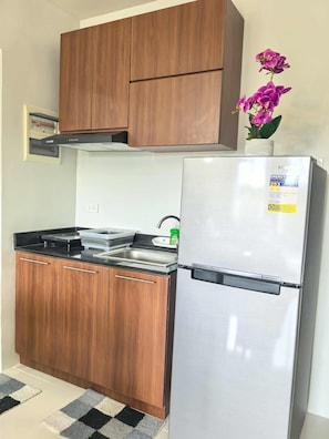 A kitchen with wooden cabinets, a stainless steel refrigerator, and a black countertop. - Stylish Condo Stay, Pool, Balcony, Gym & Near Airport (Puerto Princesa City)