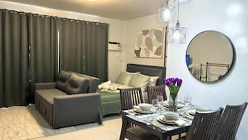 A modern hotel room with a sofa, a dining table set for two, a mirror, and a painting on the wall.