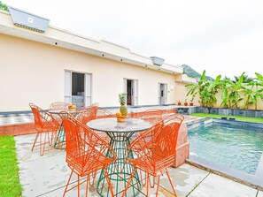 Un área junto a la piscina con una mesa redonda y sillas, una piscina pequeña y un edificio con ventanas y una puerta.