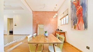 Uma área de refeições com mesa e cadeiras de madeira, uma planta em vaso e um quadro na parede.