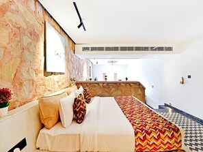 Un dormitorio con pared de piedra, una cama con ropa de cama estampada, una mesita con un florero y vistas a una zona de cocina.