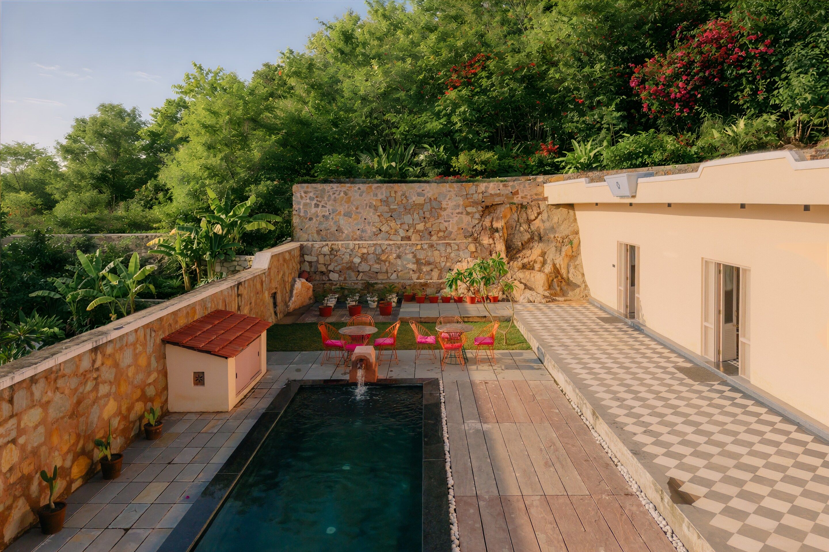 A pool area with a stone wall, a small building, and potted plants.