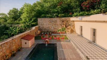 A pool area with a stone wall, a small building, and potted plants.