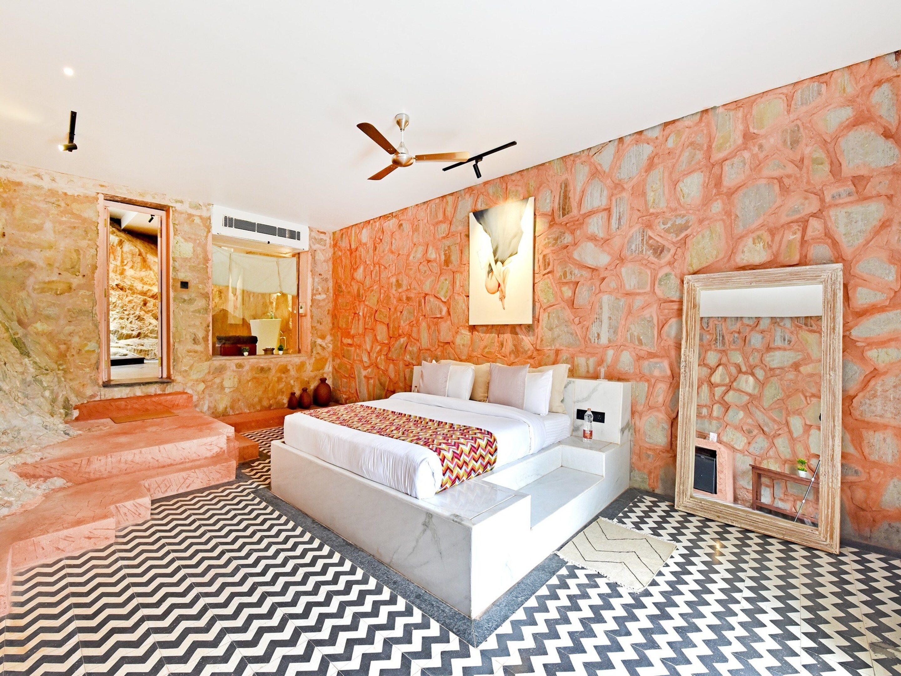 A bedroom with a large bed, a ceiling fan, stone walls, and a patterned floor.